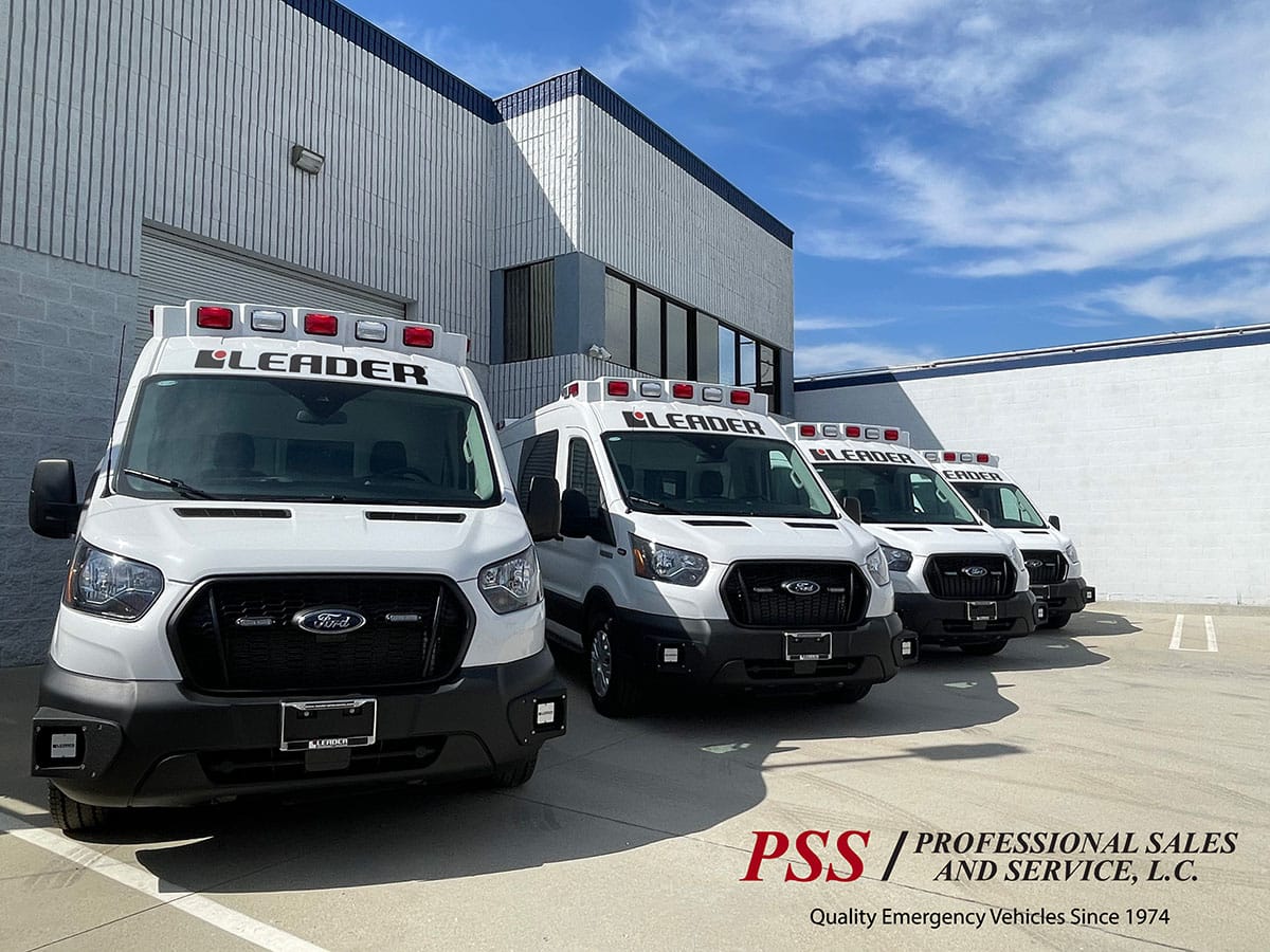 pss-leader Four white ambulances are backed up next to a building.